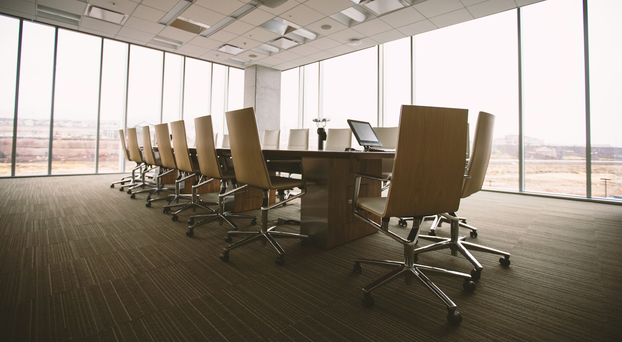 An empty boardroom with a long oval table and tall windows